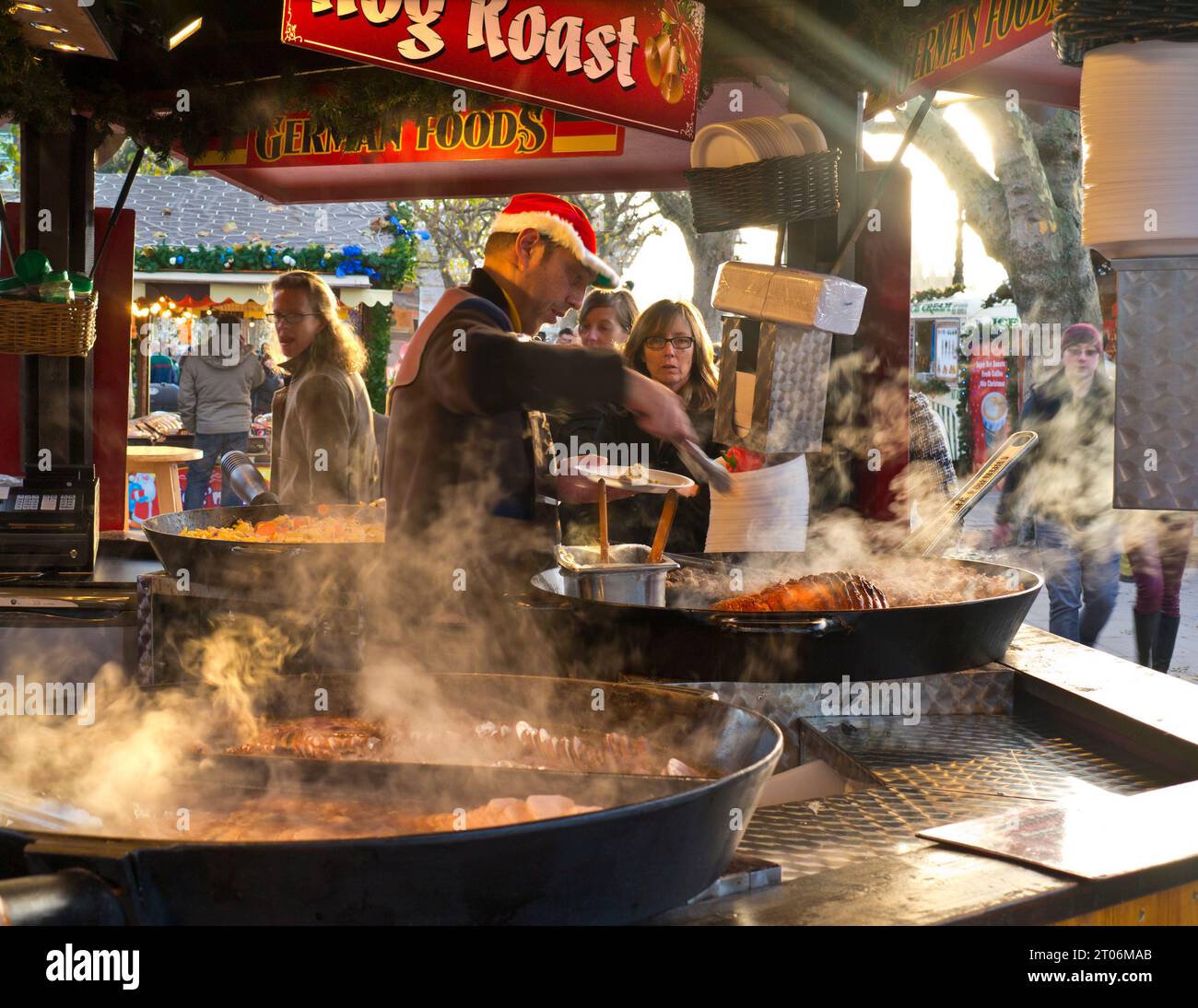 Deutscher Weihnachtsmarkt britische Southbank London Essen. Hog Roast zum Mitnehmen im Freien heiße, dampfende Würstchen und Fleisch in einem Brötchenstand, der mit Besuchern beschäftigt ist London UK London South Bank Winterfleischstände, Hog Roast heiße dampfende deutsche Spezialitäten zum Mitnehmen Fast Food Stand der Weihnachtszeit London Southbank UK Stockfoto