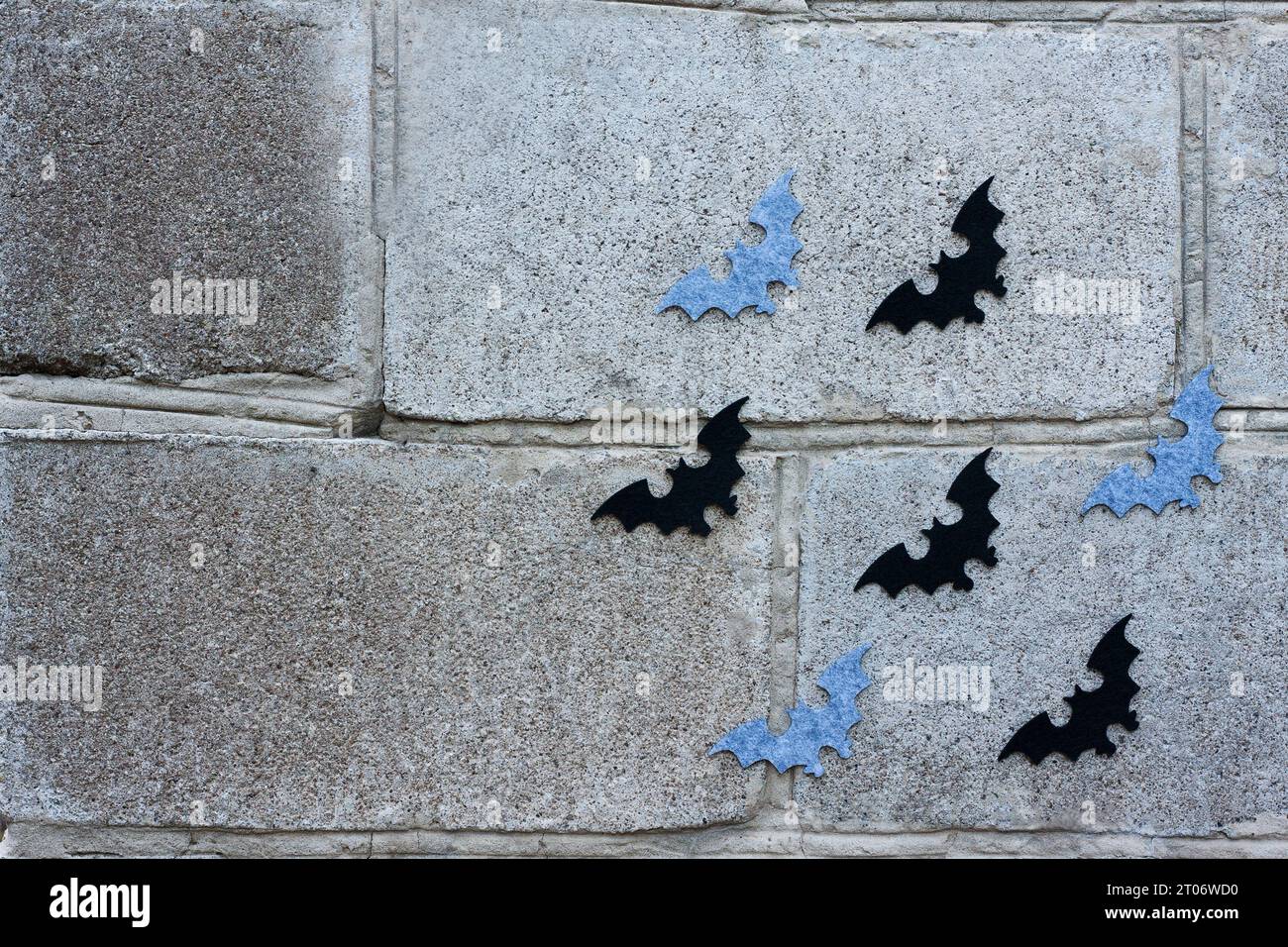 Halloween-Hintergrund. Festliche Einrichtung: Schwarze und graue Filzfledermäuse fliegen auf einer Steinmauer. Kopierbereich Stockfoto