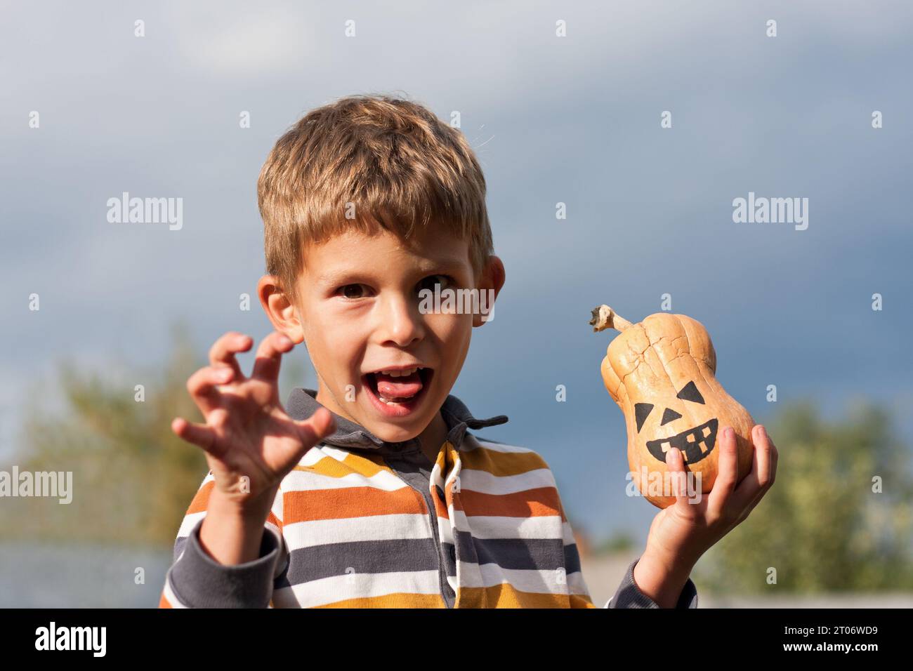 Porträt eines süßen Jungen, der eine kleine Laterne in den Händen hält und grimmig ist. Hintergrund blauer Himmel, heller oktobertag. Frohes halloween. Stockfoto