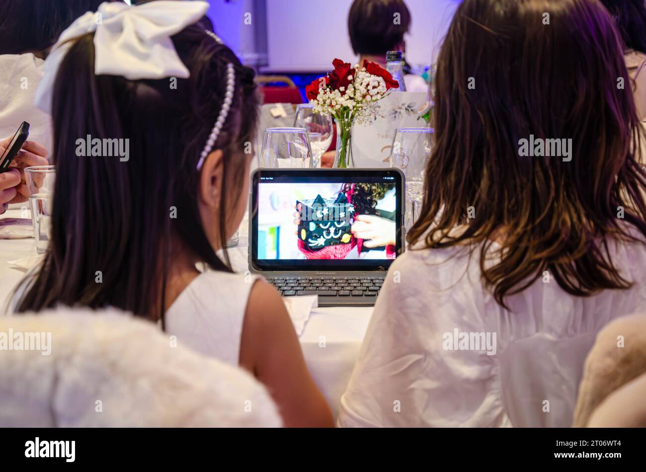 Ein paar junge Mädchen werden auf einer Party unterhalten und sehen fernsehsendungen auf einem kleinen Laptop-Tablet-Computer, der hinter ihm zu sehen ist Stockfoto