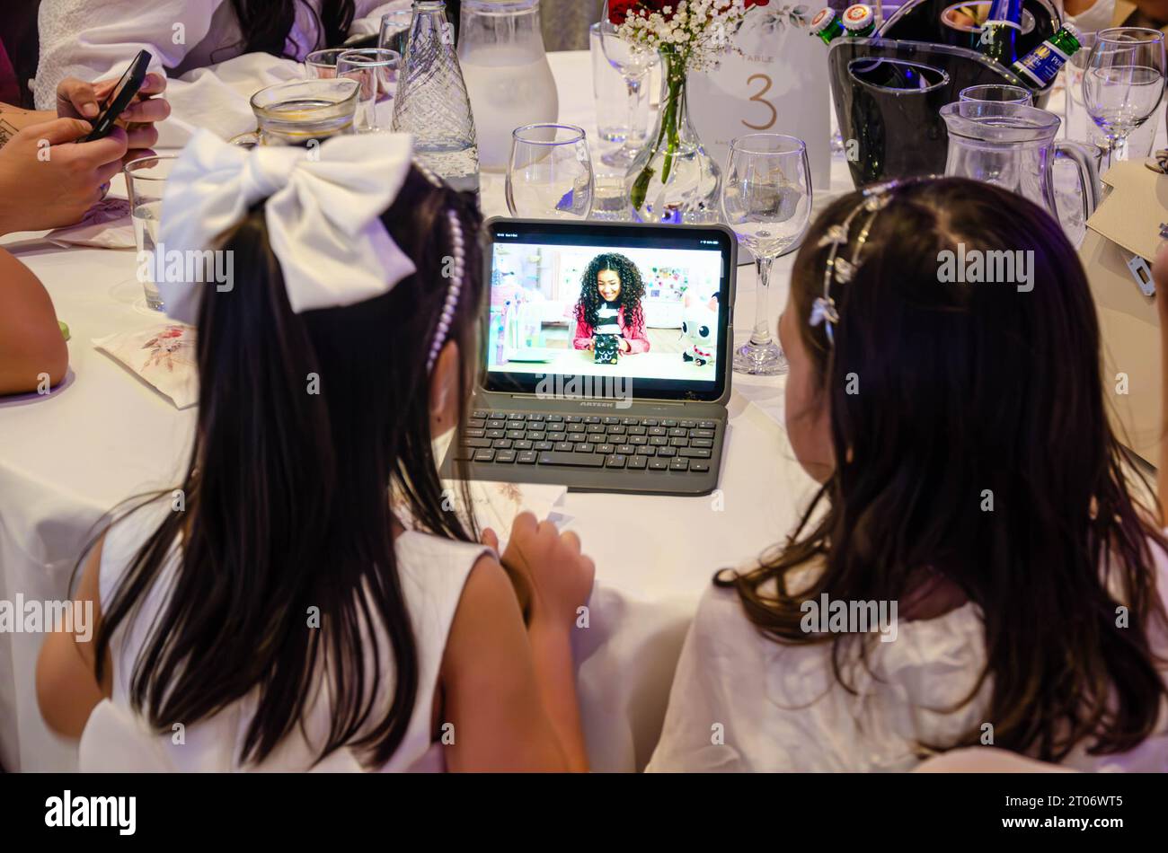 Ein paar junge Mädchen werden auf einer Party unterhalten und sehen fernsehsendungen auf einem kleinen Laptop-Tablet-Computer, der hinter ihm zu sehen ist Stockfoto