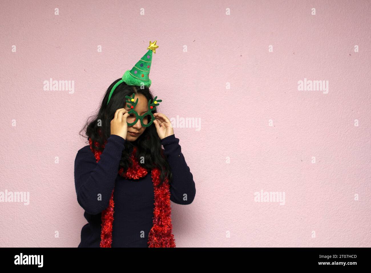 Junge Latina Teenager mit Weihnachtsmütze und -Brille zeigt ihre Unzufriedenheit, Traurigkeit und Wut, als sie im Dezember Weihnachten hasst Stockfoto