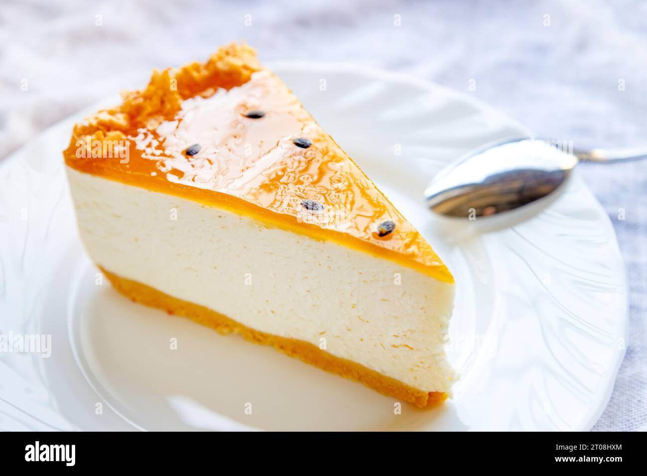 Köstliche frisch gebackene mehrlagige Mango Passionsfrucht Käsekuchenscheibe mit Fruchtgelee auf weißem Teller Nahaufnahme. Stockfoto