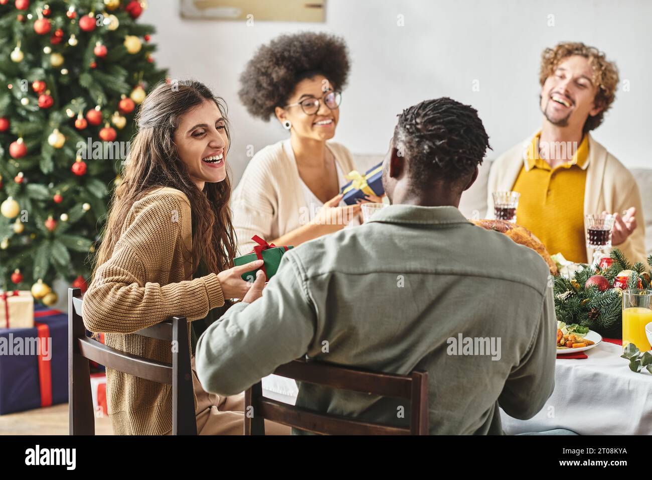 Große, fröhliche Familie lacht und sieht sich beim Weihnachtsessen an, während sie Geschenke austauscht Stockfoto