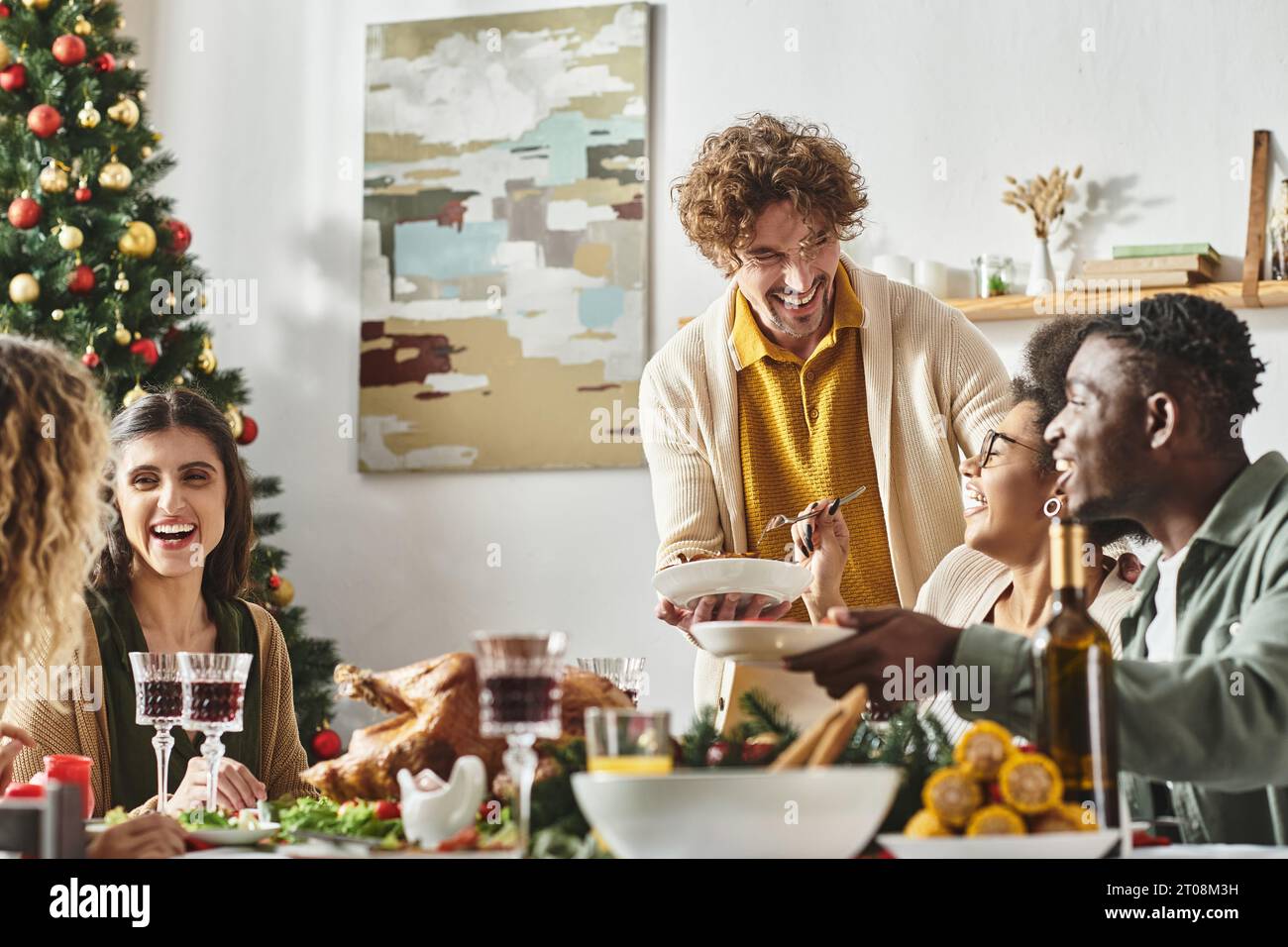 Große, fröhliche, multikulturelle Familie, die am Weihnachtstisch sitzt, lacht und die Feiertage genießt Stockfoto