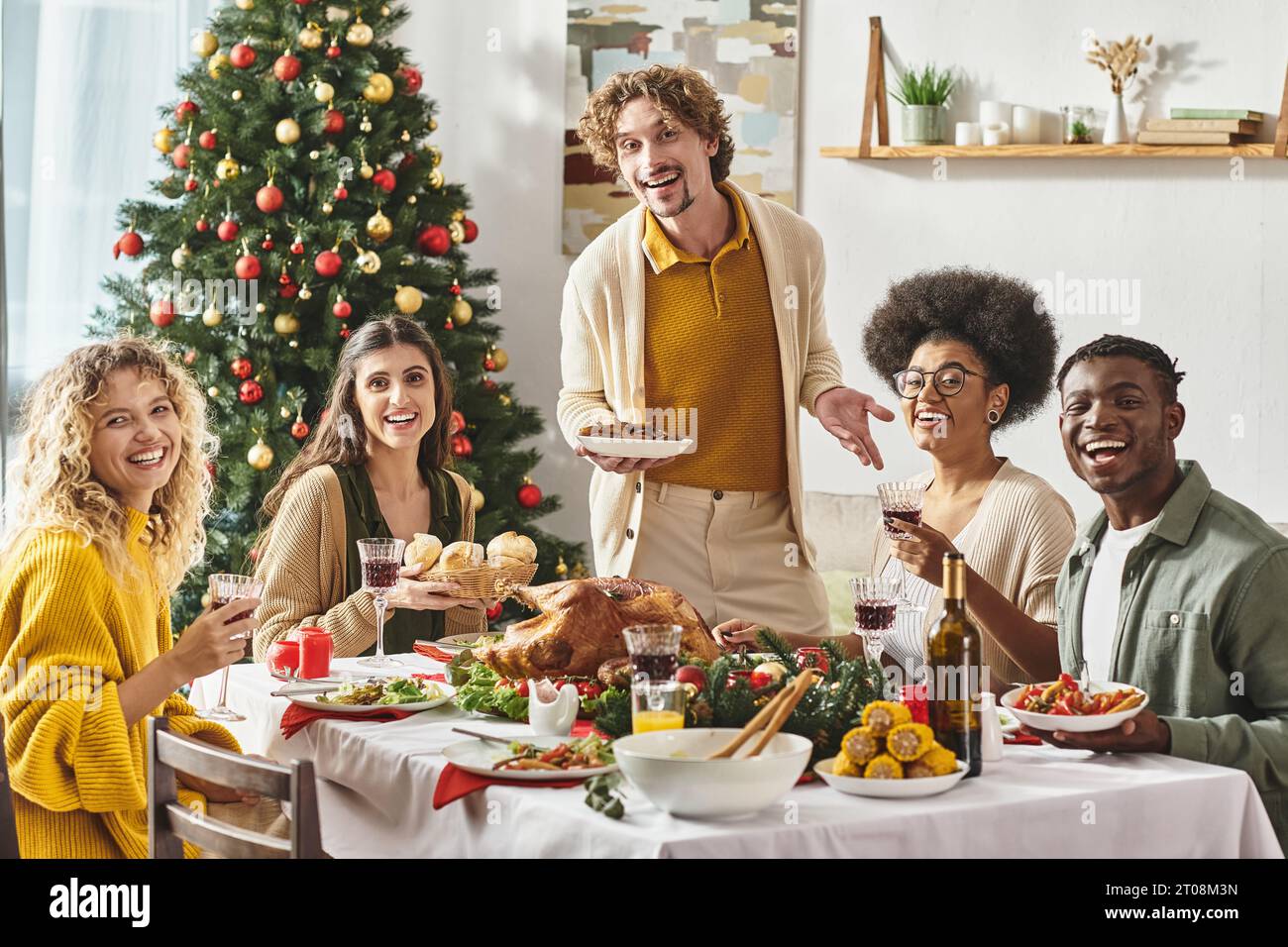 Fröhliche multikulturelle Familie, die Weihnachten mit Wein und einem Lächeln in die Kamera genießt Stockfoto