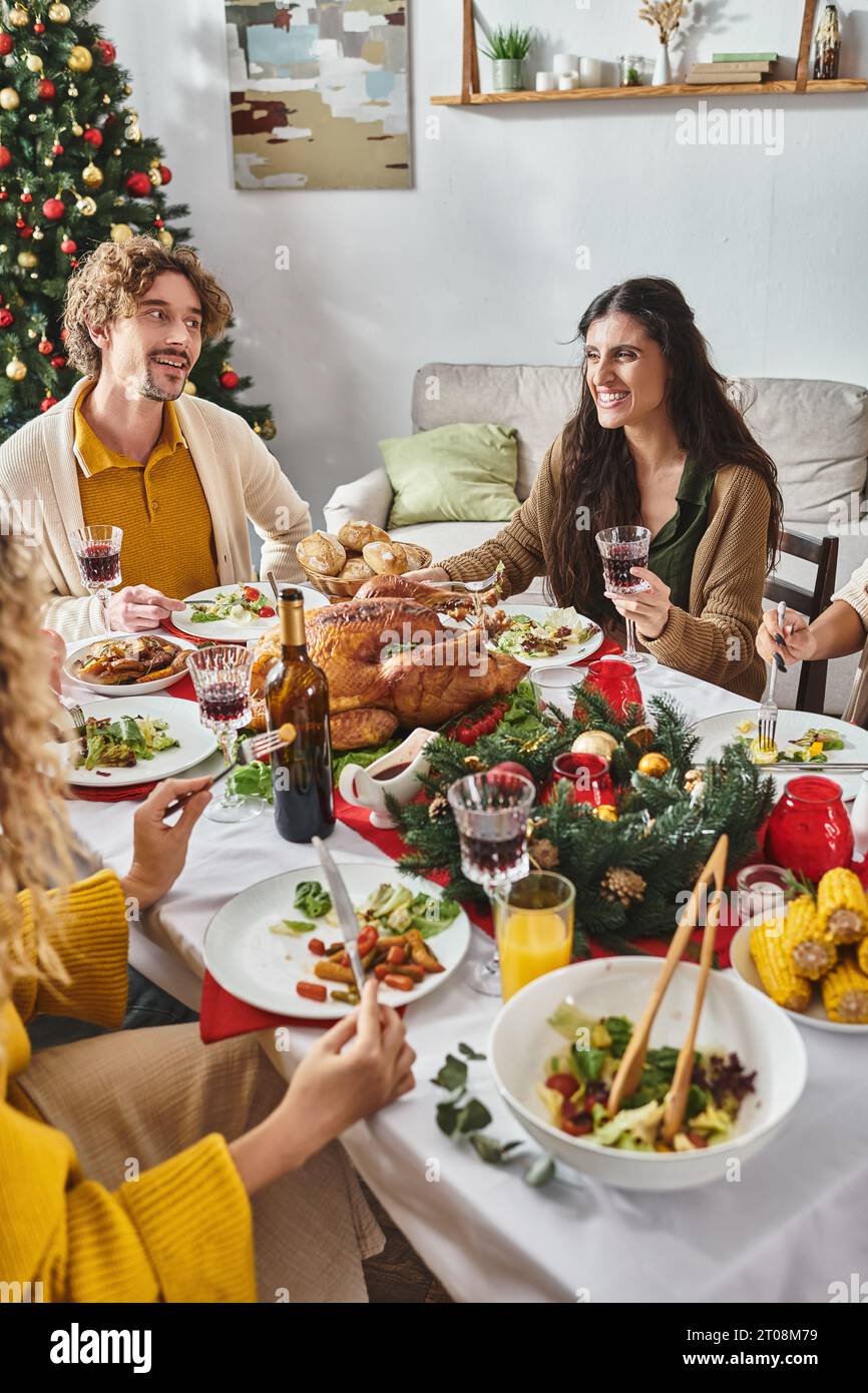 Zugeschnittene Ansicht multirassische Familie genießt ein Mittagessen im Urlaub und lächelt mit Weihnachtsbaum im Hintergrund Stockfoto