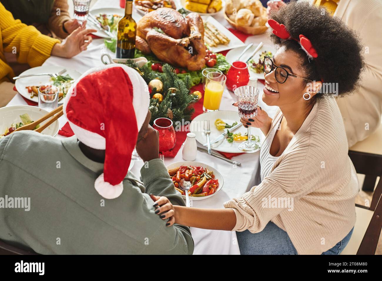 Fröhliches afroamerikanisches Paar am Weihnachtstisch mit ihrer multiethnischen Familie, Hand an Schulter Stockfoto