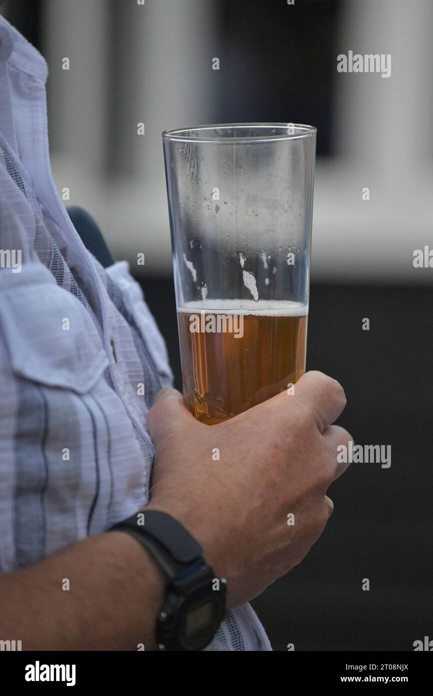 Männliche Hand, die ein Glas halb voll Bier hält Stockfoto