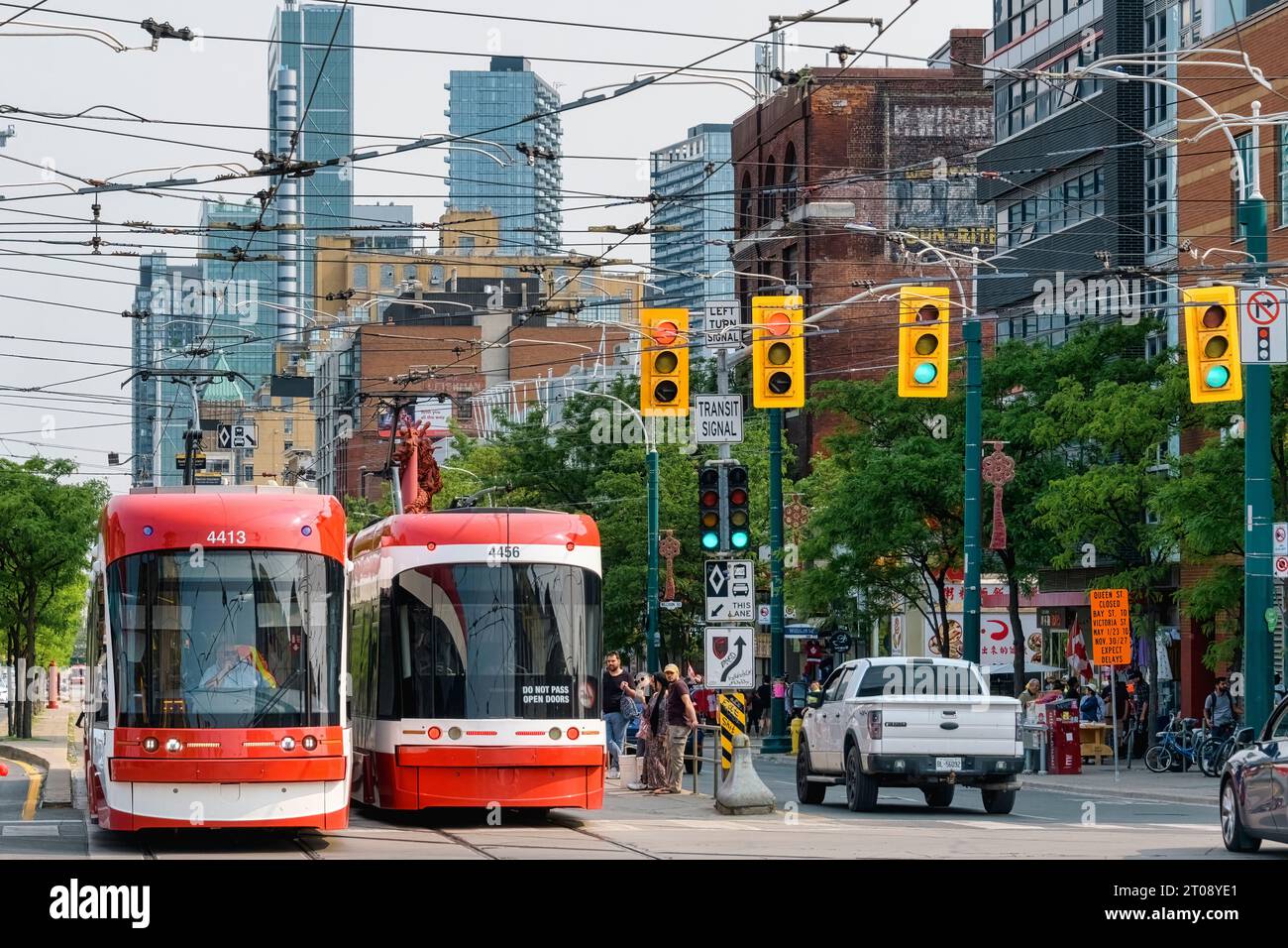 Toronto, Kanada - 4. Juni 2023: Zwei rot-weiße Straßenbahnbusse fahren über eine Stadtstraße. Die Fahrzeuge fahren unter den Oberleitungen mitten im Stadtverkehr Stockfoto