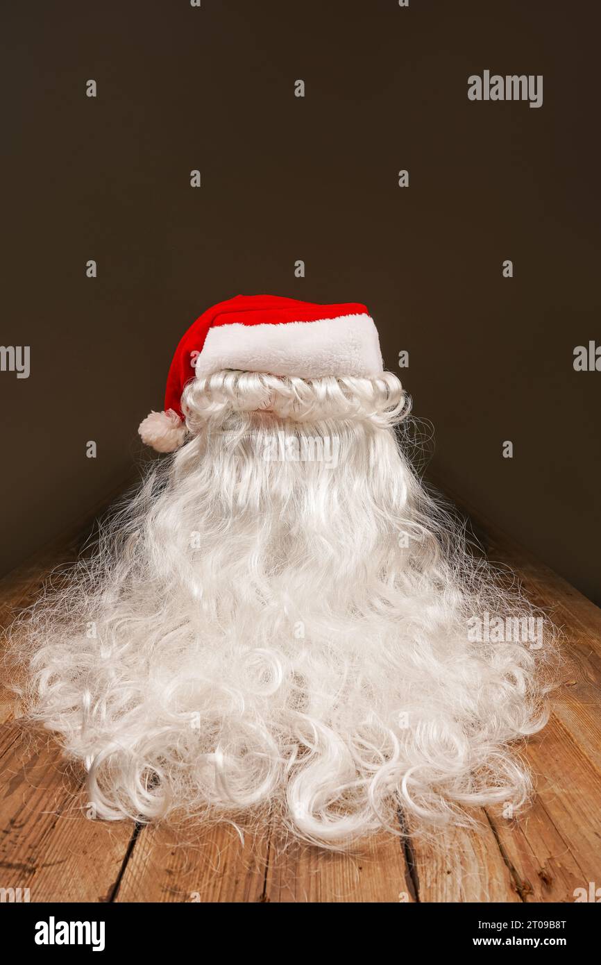 Weihnachtsmann Hut und Bart auf hölzernem Hintergrund. Symbolik der Neujahrsfeiertage. Weihnachts- und Neujahrskonzept. Wechsel der Kleidung, Veränderung des Bildes Stockfoto