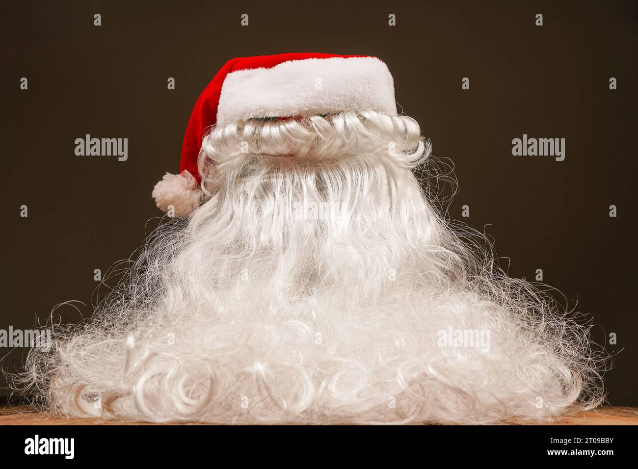 Weihnachtsmann Hut und Bart auf hölzernem Hintergrund. Symbolik der Neujahrsfeiertage. Weihnachts- und Neujahrskonzept. Wechsel der Kleidung, Veränderung des Bildes Stockfoto