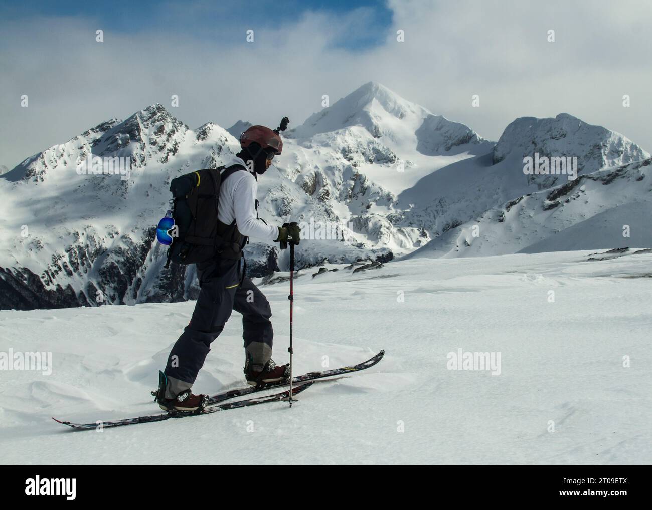 Seitenansicht eines schwarzen Skifahrers in warmen Skianzügen und mit Rucksack, der entlang des verschneiten Berges vor wolkenlosem blauen Himmel auf Ushuaia Argentina schlendert Stockfoto
