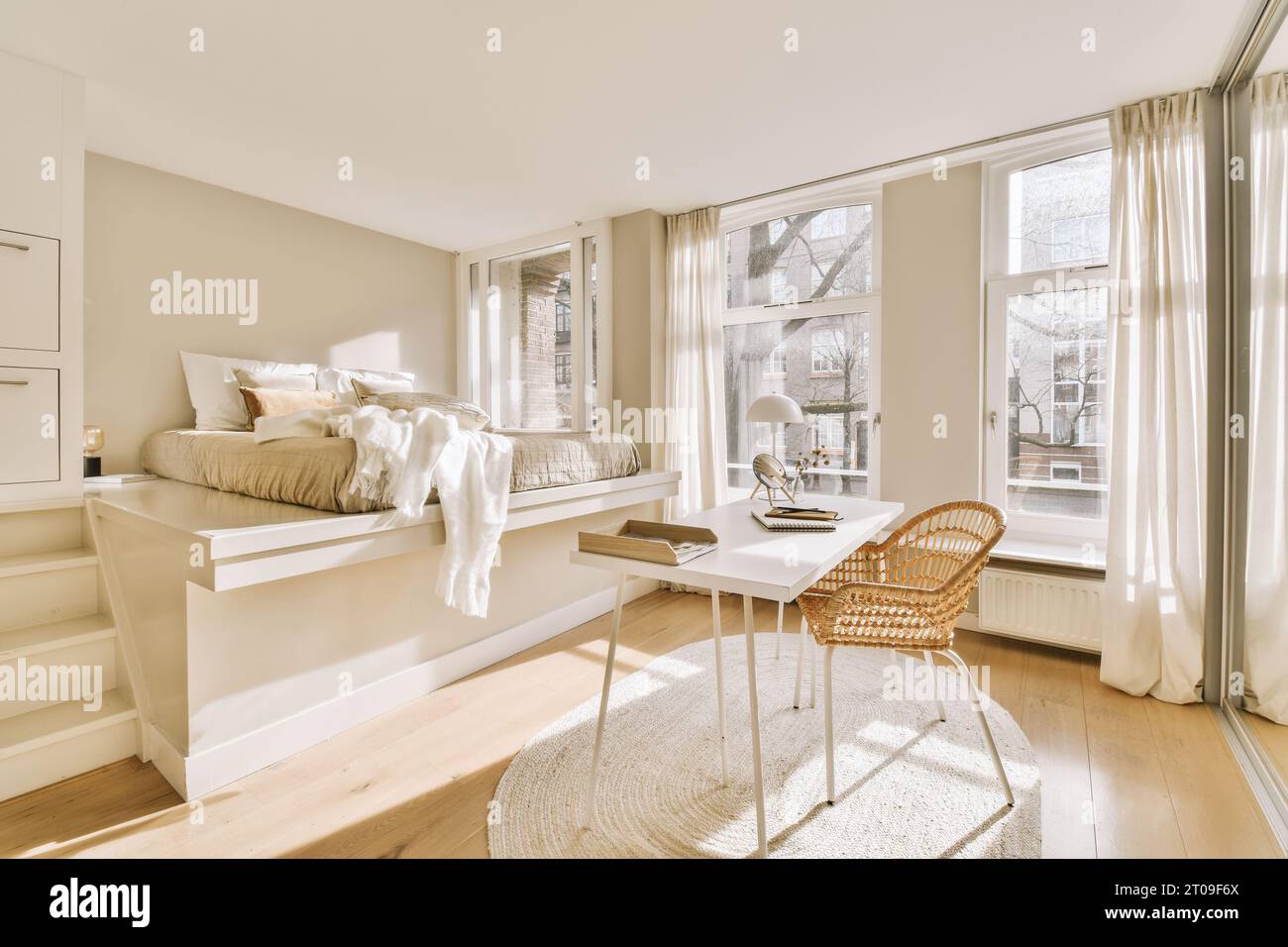 Inneneinrichtung des modernen Schlafzimmers mit Schreibtisch und Stuhl vor dem Bett durch große Fenster an sonnigen Tagen Stockfoto