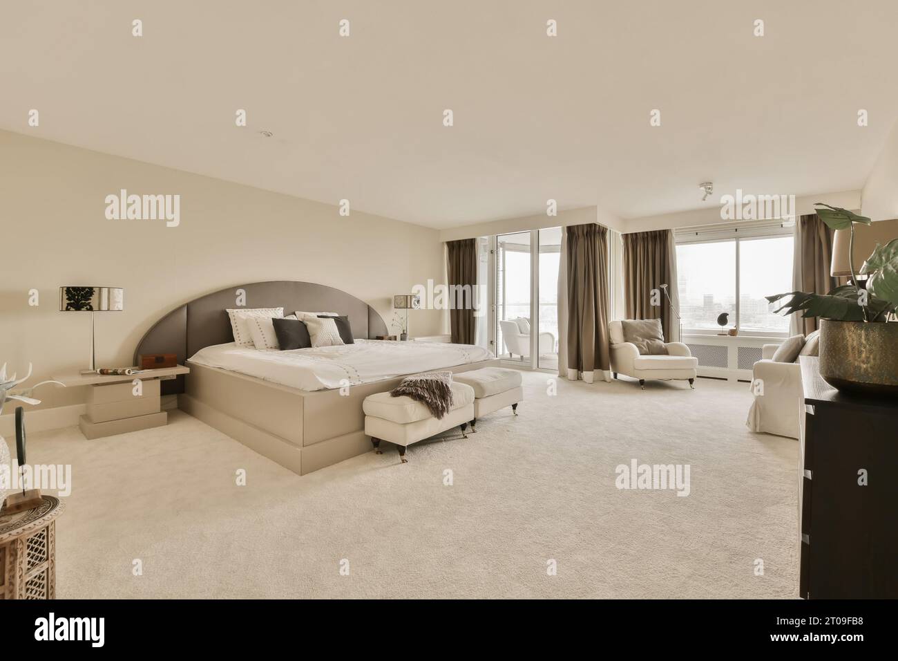 Das Innere des geräumigen, modernen weißen Schlafzimmers mit Bett und Sessel vor der Wand Stockfoto