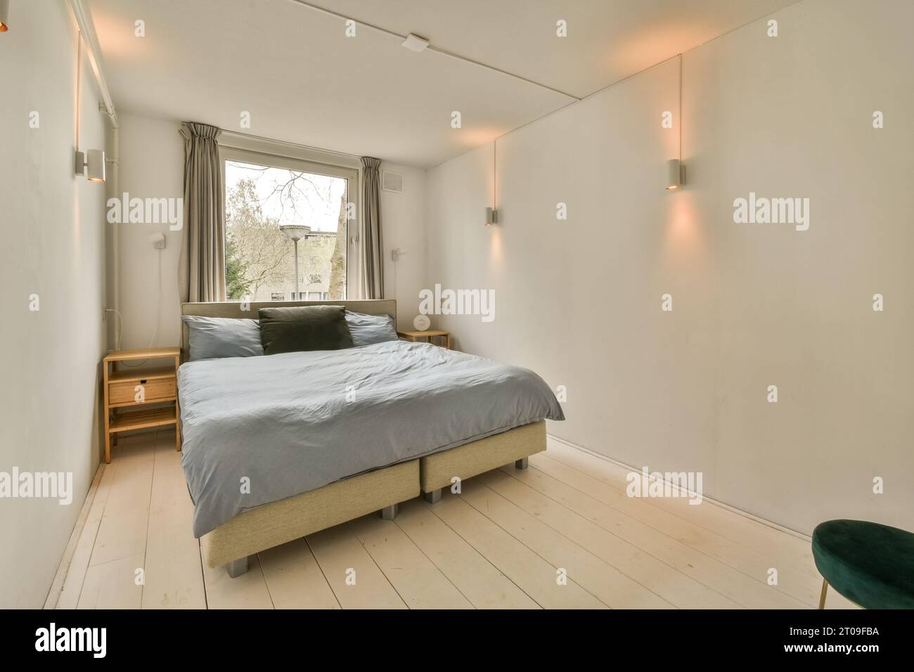 Innenraum des beleuchteten modernen Schlafzimmers mit Bett vor dem Fenster zu Hause mit weißer Wand Stockfoto