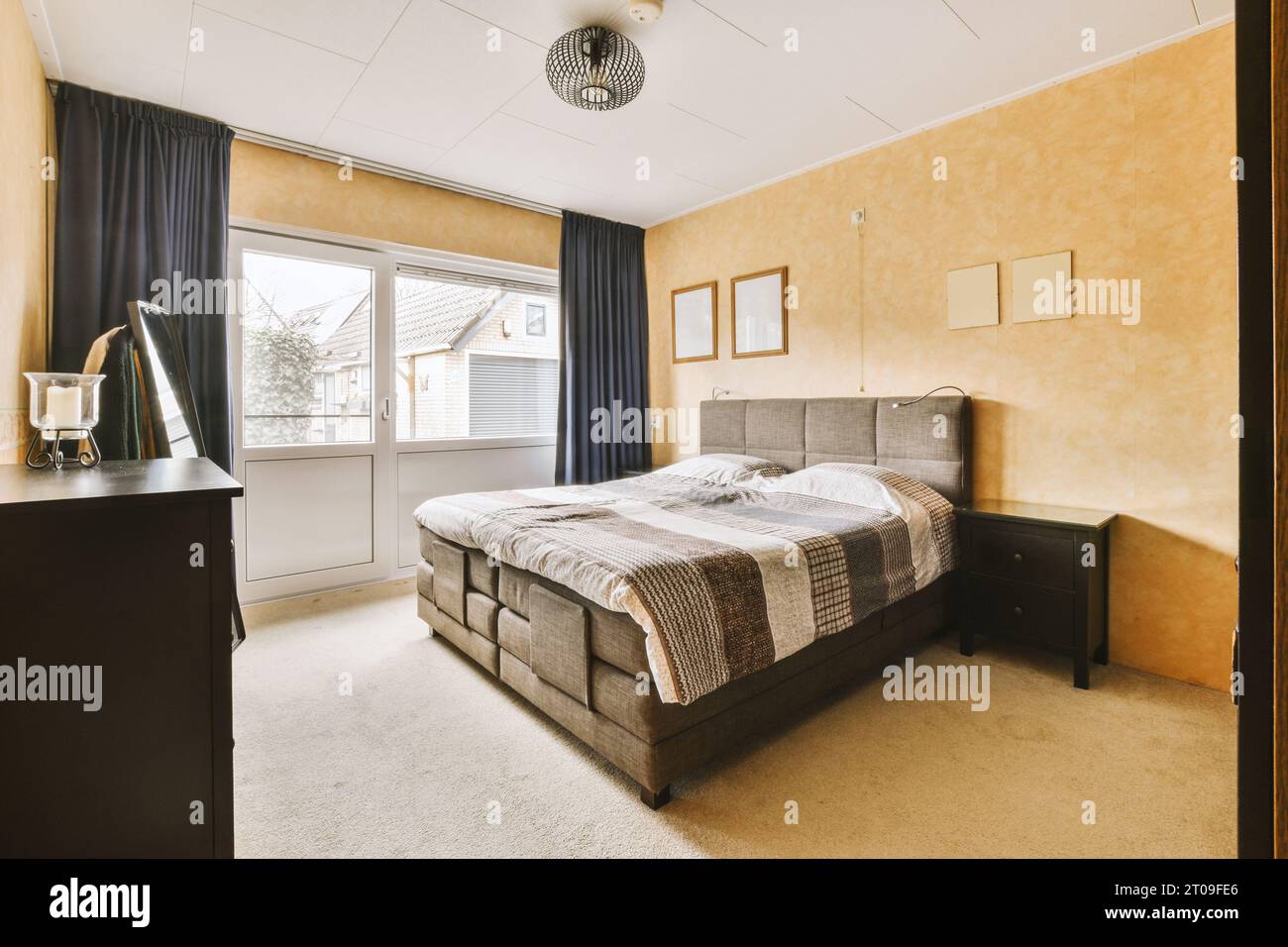 Innenraum des Schlafzimmers mit komfortablem Bett vor der orangen Wand in einem modernen Haus mit großem Fenster Stockfoto