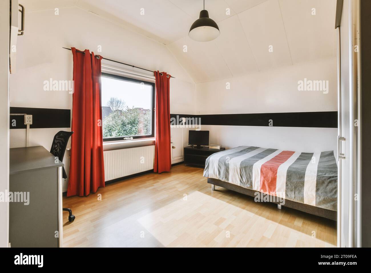 Inneres des Schlafzimmers mit Bett vor dem Fenster mit roten Vorhängen in geräumigem Apartment Stockfoto