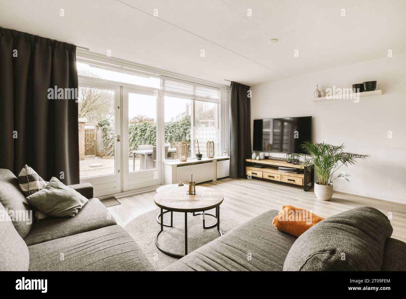 Komfortables Sofa und Couchtisch vor dem Fernseher durch großes Fenster im modernen Wohnzimmer Stockfoto