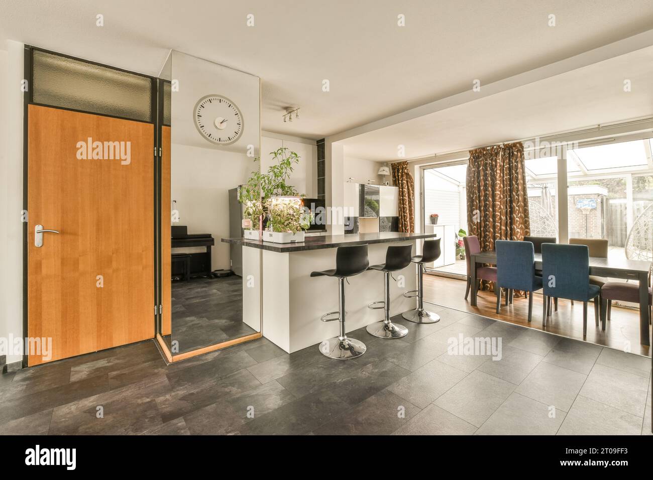 Esstisch und Stühle sind vor der Kücheninsel in einem modernen Apartment vor großen Fenstern angeordnet Stockfoto