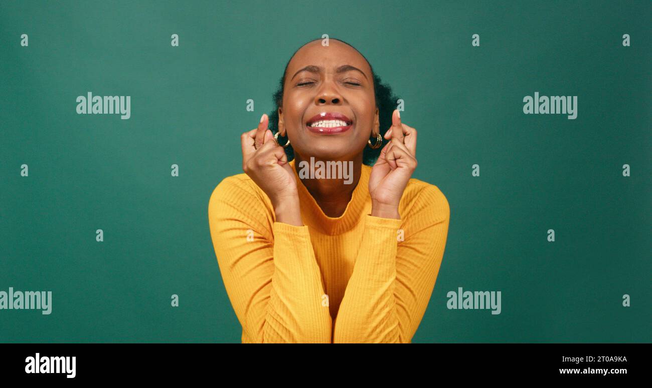 Schöne junge Frau mit gekreuzten Fingern, wünscht und hofft, grünes Studio Stockfoto