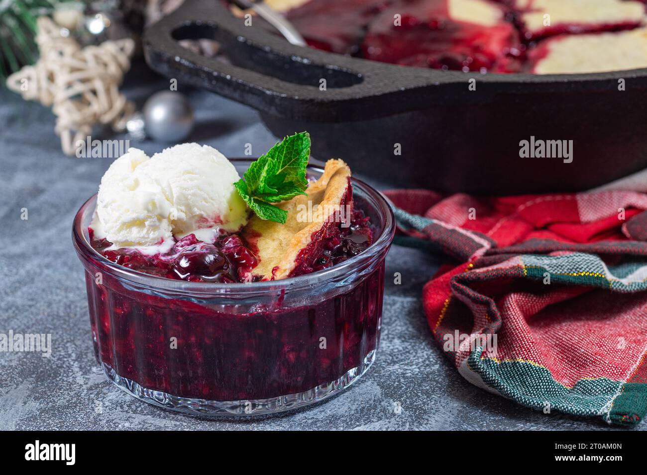 Hausgemachter Beeren-Schuster in Glas-Ramekin mit Eis und in gusseiserner Pfanne, Weihnachtsdekoration auf Hintergrund, horizontal Stockfoto