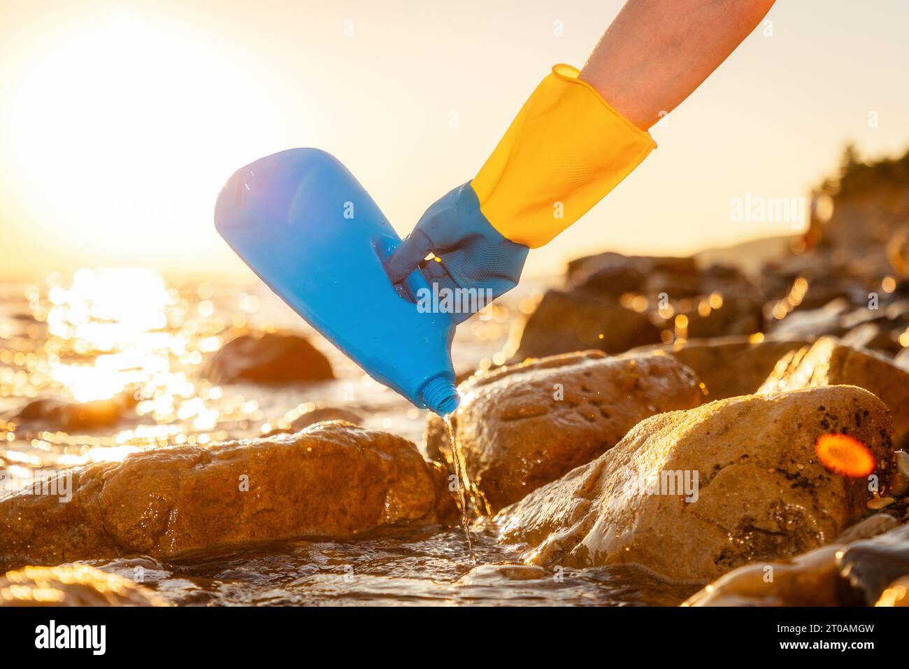 Ökologische Katastrophe. Nahaufnahme der Freiwilligen Hand in Gummihandschuhen nimmt blaue Plastikflasche an der wilden Küste auf. Konzept der Säuberung der Küste und Save p Stockfoto