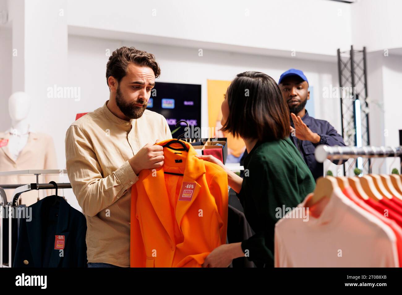 Der Sicherheitspersonal der Mall beruhigt zwei Kunden, die während des Verkaufs um Kleidungsstücke kämpfen. Leute, die sich im Bekleidungsgeschäft streiten, am Black Friday verrückt werden, nach Schnäppchen suchen Stockfoto