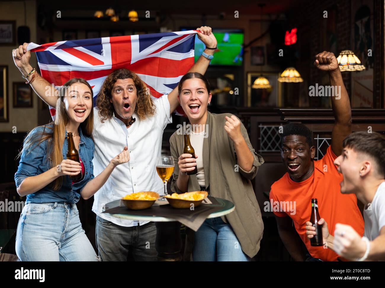 Begeisterte diverse Fußballfans mit der britischen Flagge, die den Sieg mit einem Pint Bier und Chips im Pub feierte Stockfoto