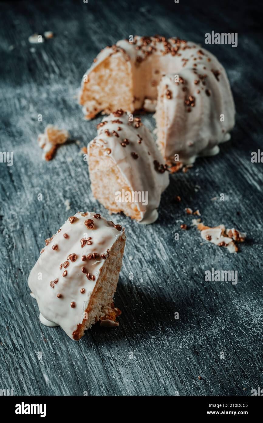 Einige Bruchstücke eines gugelhupf-Kuchens, bedeckt mit einem Vanillefrosting, auf einem grauen rustikalen Holztisch Stockfoto