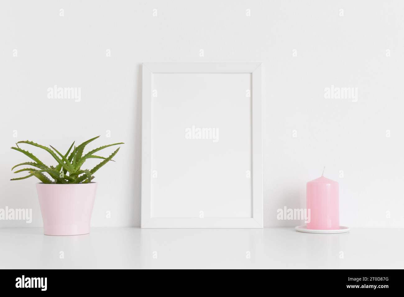 Weißes Rahmenmockup mit einer saftigen Pflanze und einer Kerze auf einem weißen Tisch. Hochformat. Stockfoto