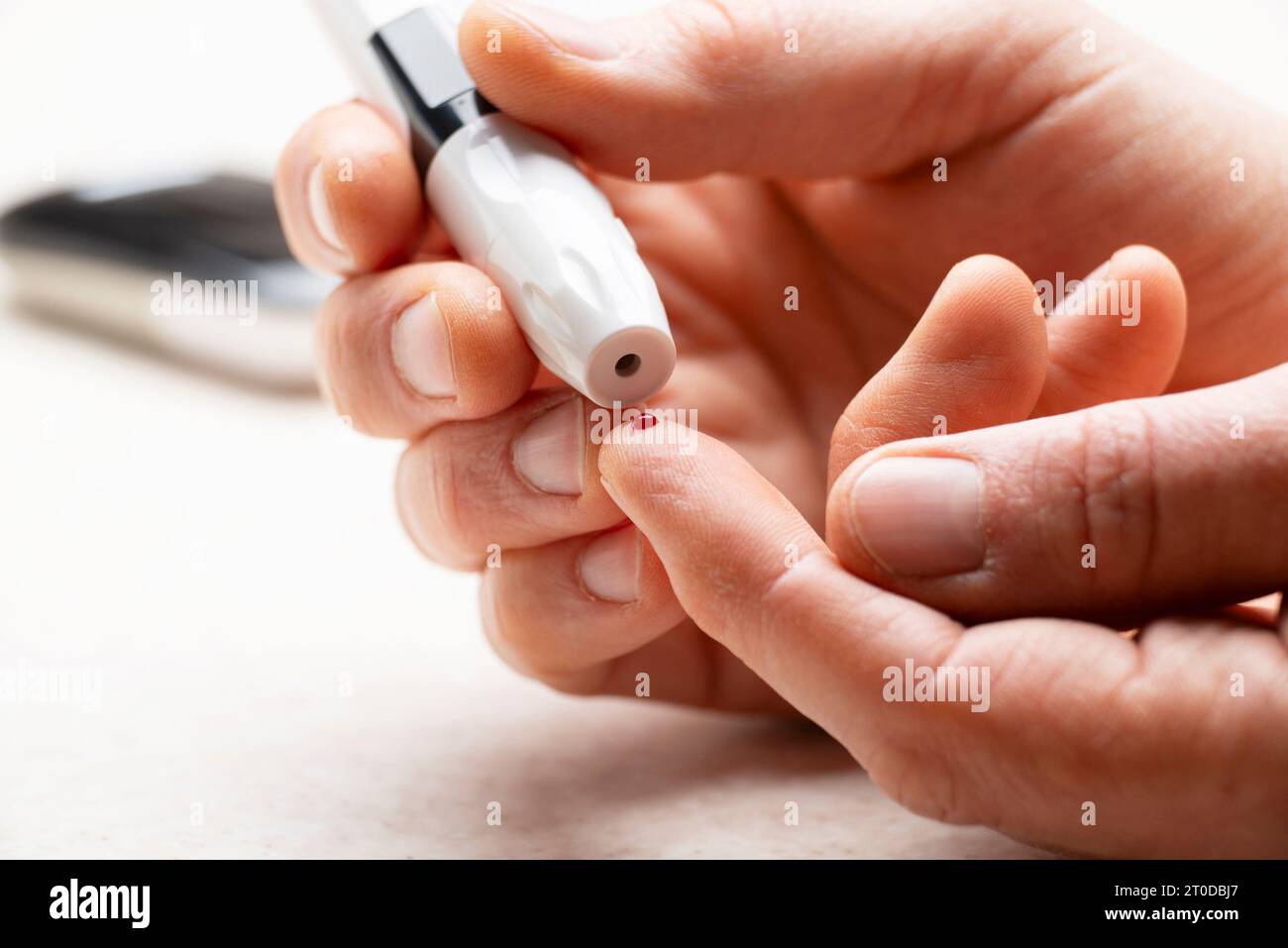 Kaukasischer Mann mittleren Alters hat sich seinen Finger für den Glukosetest zu Hause mit Messgerät und Zubehör im Hintergrund durchbohrt Stockfoto