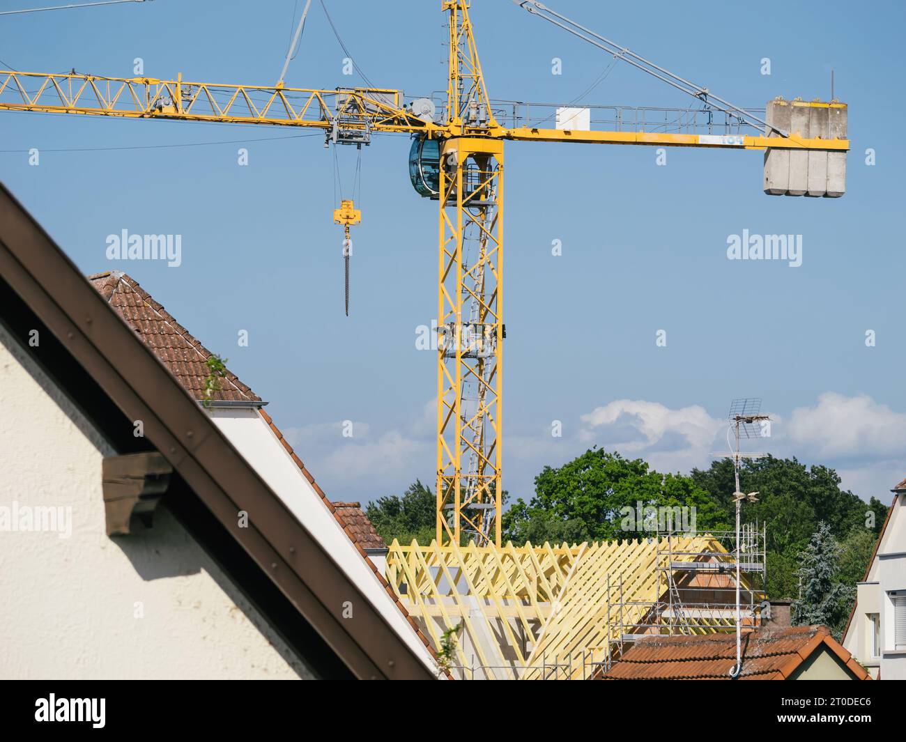 Durch ein Teleobjektiv erfasst, entfaltet sich ein Panorama von Dächern, unterbrochen von einem hochaufragenden Kran, der aktiv am Bau eines Gebäudes beteiligt ist. Stockfoto