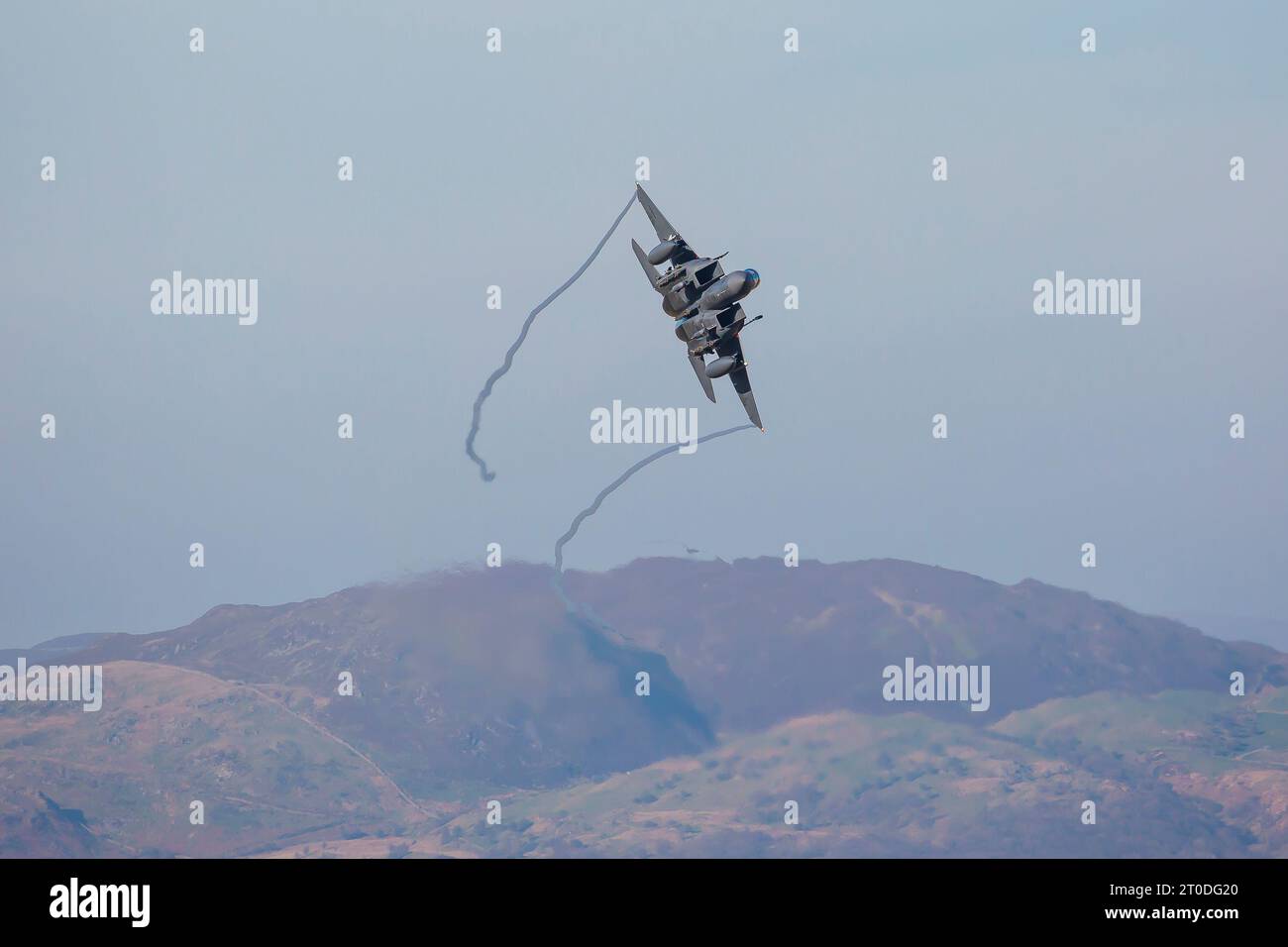 Amerikanisches Militärflugzeug F15 fliegt auf einem Trainingsflug durch einen blauen Himmel mit walisischen Hügeln im Hintergrund Stockfoto