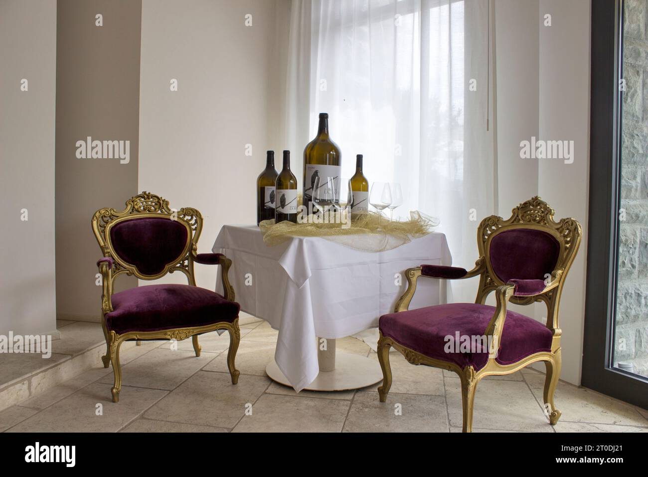 In diesem gemütlichen Speisesaal hängt eine lebendige Tischdecke über einem stabilen Tisch mit Stühlen, während Weinflaschen und eine Vase frischer Flocken vorhanden sind Stockfoto