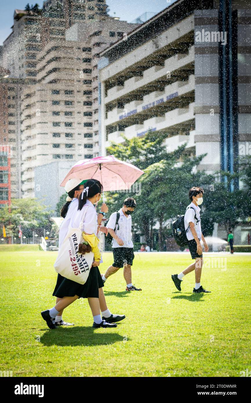 Thailändische Universitätsstudenten schlendern über den Hauptrasen der Srinakharinwirot University Bangkok, Thailand, und werden von Gartenregnern nass. Stockfoto