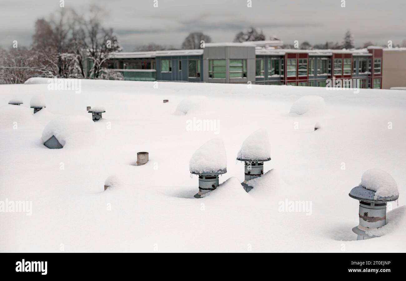 Dachentlüftungen mit Schnee auf einem Gebäude mit Flachdach. Winterdachszene mit Metallventilatoren, eingeschneit und mit tiefem Schnee bedeckt. Da Stockfoto