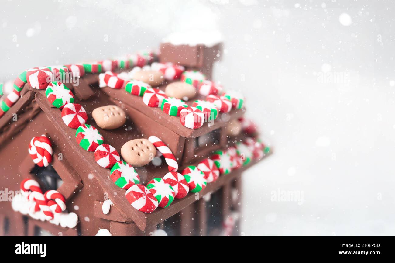 Lebkuchenhaus aus Lehm mit Schneehintergrund. Hintergrund für DIY-Weihnachten oder Weihnachten. Miniatur-Tonhaus mit roten und grünen Bonbons, Bonbons, b Stockfoto