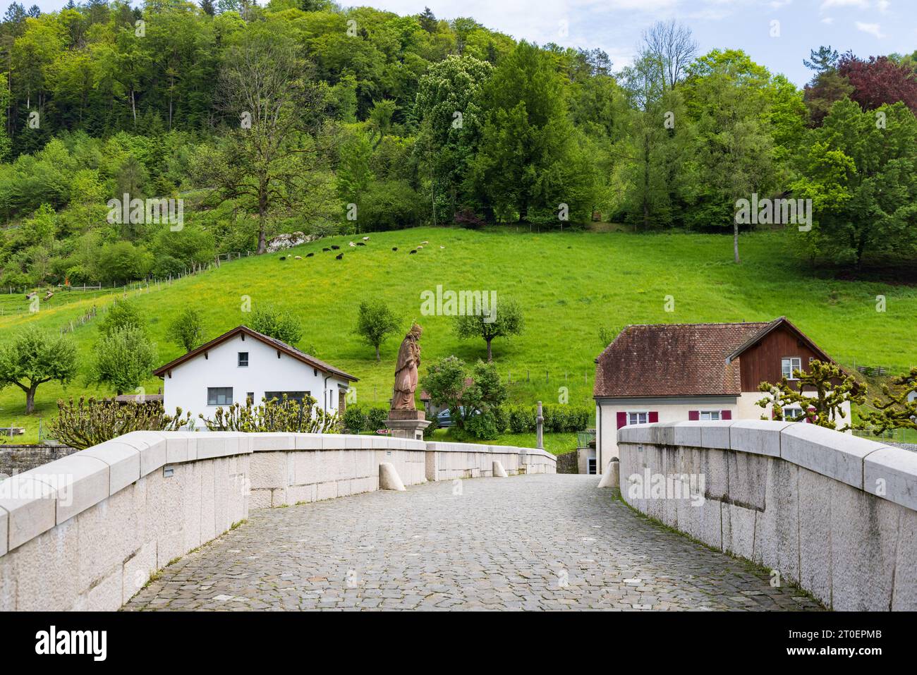 St-Ursanne, Schweiz - 15. Mai 2023: Eingangsbrücke mit historischer saint-Skulptur überquert den Doubs im malerischen Dorf Saint-Ursanne im Kanton Jura destrikt Porrentruy in der Schweiz Stockfoto