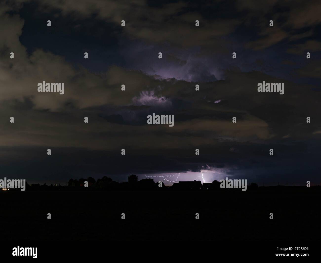 Nachts schießen Blitze aus einer fernen Gewitterwolke auf die Erde Stockfoto