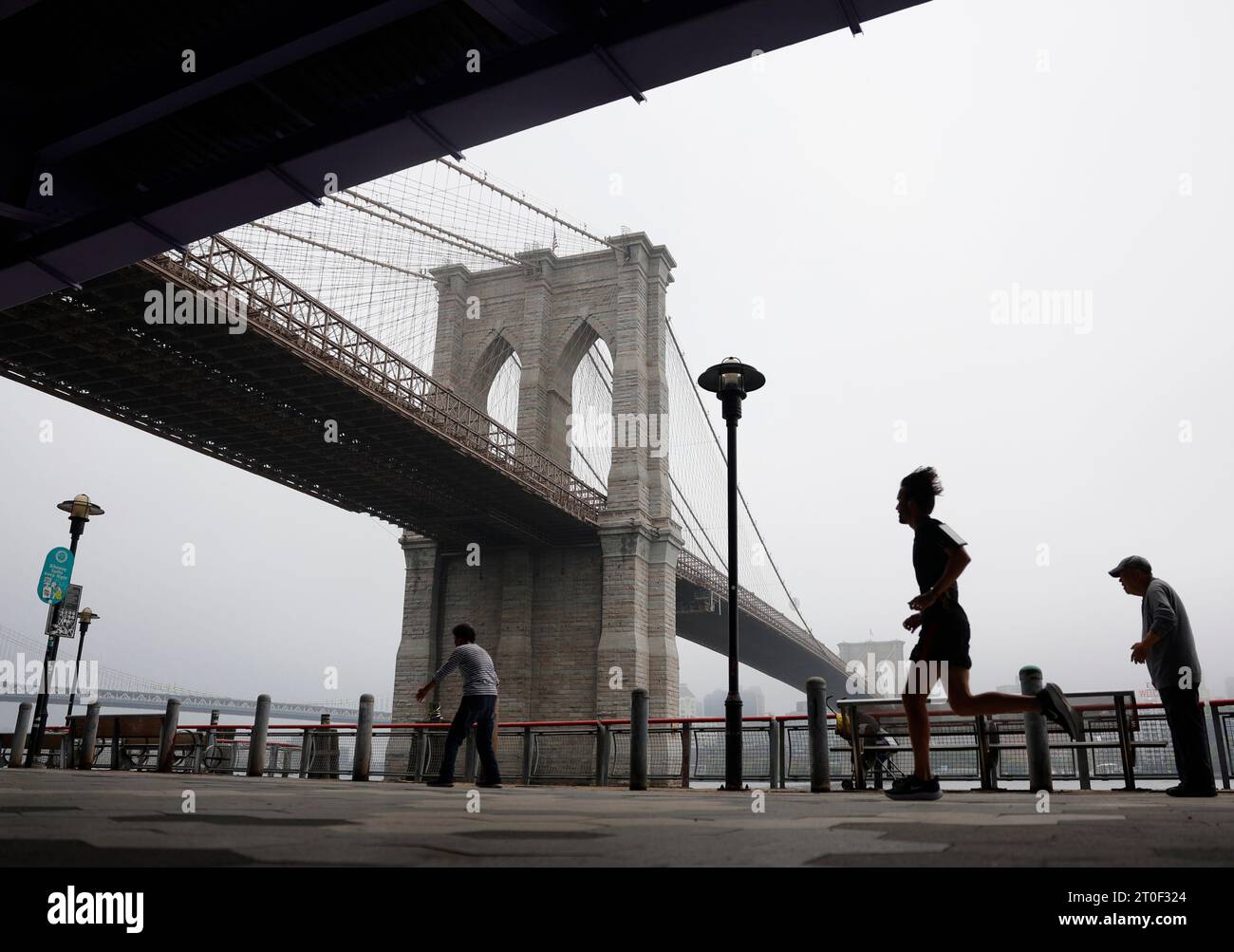 New York, Usa. Oktober 2023. Ein Läufer joggt an Fußgängern vorbei, während leichter Regen in der Nähe der Brooklyn Bridge am Freitag, den 6. Oktober 2023 in New York City durch den Nebel fällt. Foto: John Angelillo/UPI Credit: UPI/Alamy Live News Stockfoto