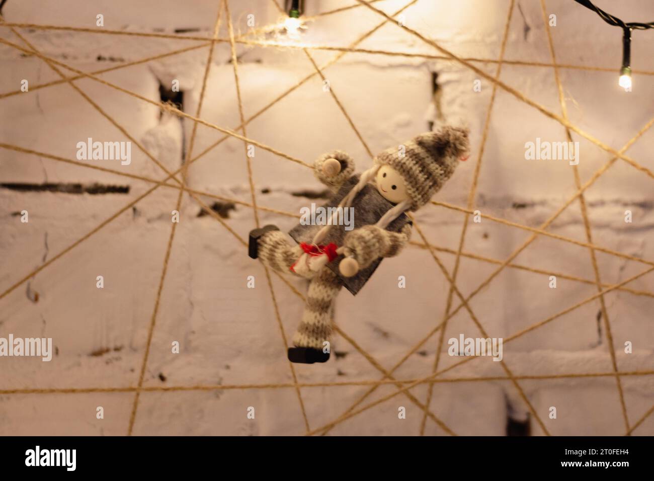 Kleine Puppe mit Nadel am Seil. Festliches Streichkunstkonzept. Girlande und Puppe auf Wunschtafel. Weihnachtsdekoration. Gemütliches Wohndekor. Einrichtung des Hauses. Stockfoto