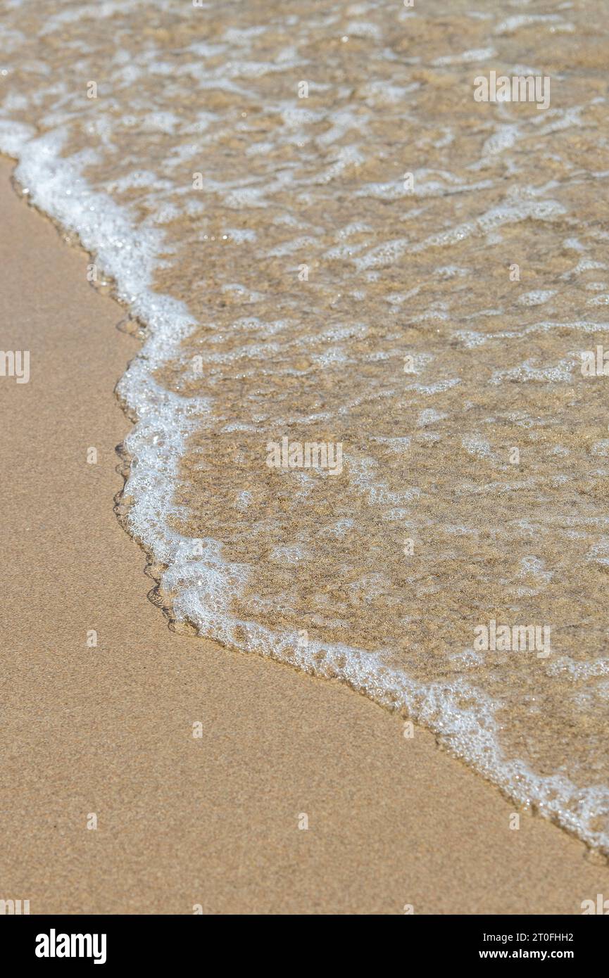 Wavelet auf einem mediterranen Sandstrand. Schäumende kleine Welle an einem tropischen Sandstrand. Stockfoto