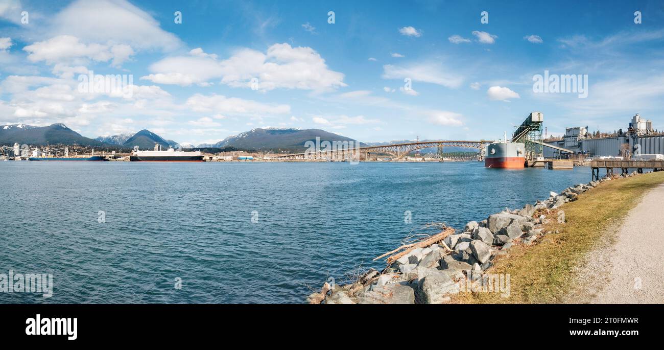 Frachtschiff, das am Hafenterminal vor der Brücke angedockt ist, und verankerte Containerschiffe. Seetransportpanorama mit Hafenanlage. Eisenarbeiter Memoria Stockfoto