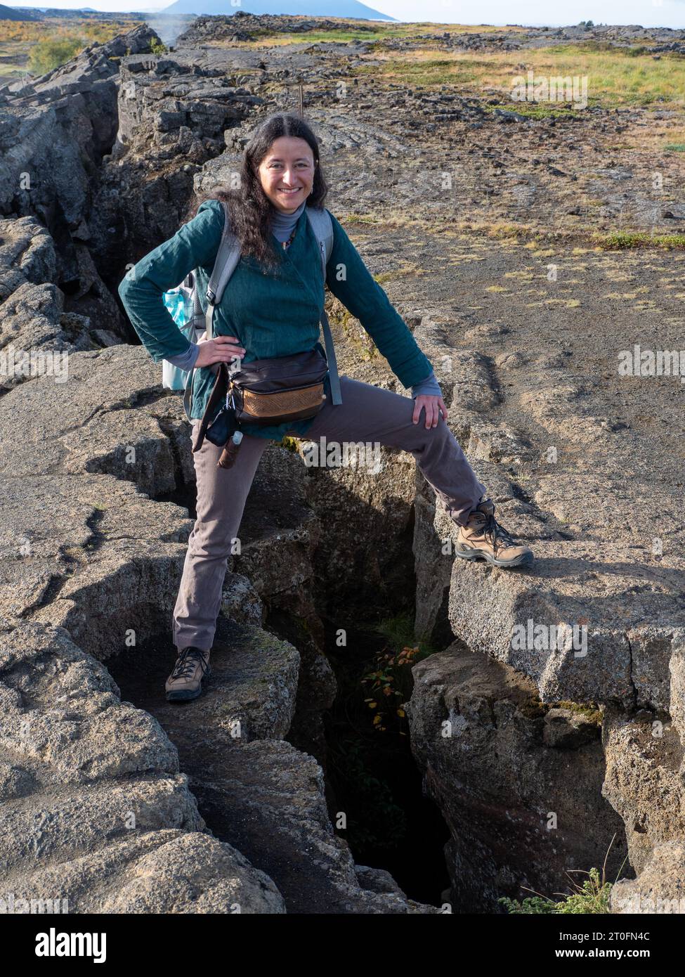 Eine lächelnde Frau, die eine Verlängerungsfraktur bei Grjótagjá zwischen nordamerikanischen und europäischen Platten, Island, überspannt Stockfoto