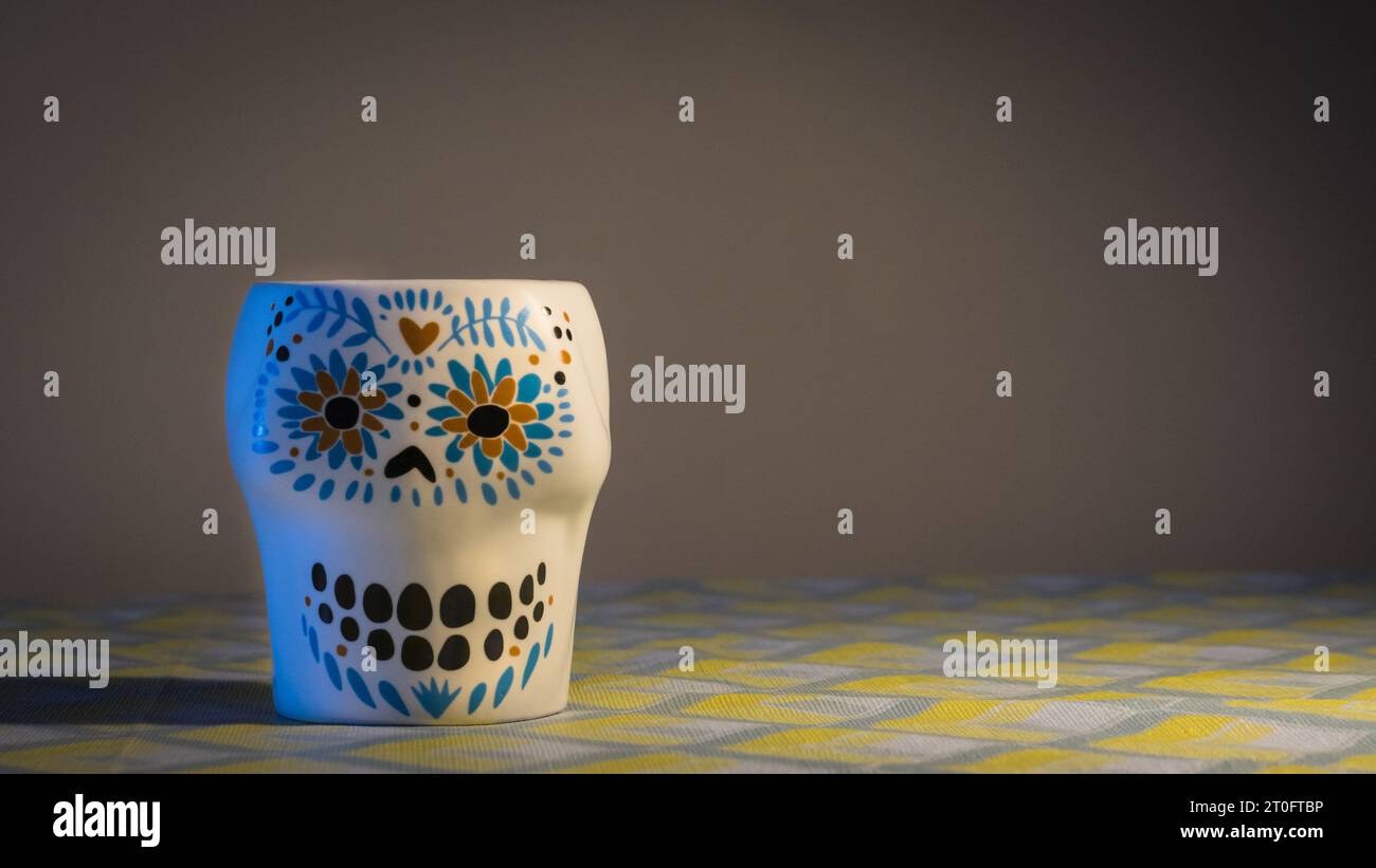 Ein Becher mit Schädelgesicht setzt vor einem geheimnisvollen grau-schwarzen Hintergrund ein markantes Statement, das makabere Ästhetik mit moderner Raffinesse verbindet Stockfoto