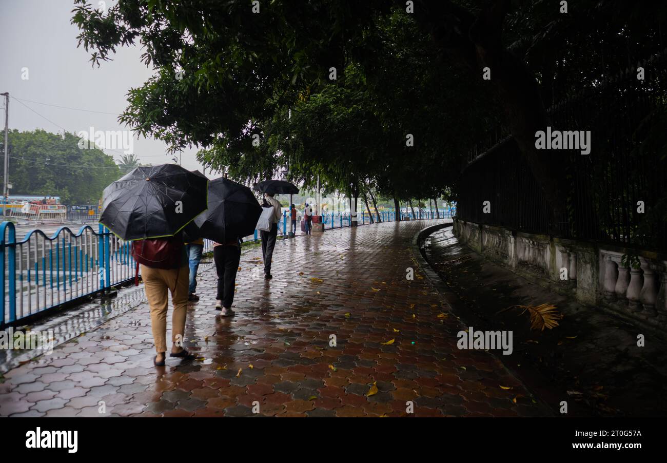Menschen, die mit einem Regenschirm auf einem regennassen Fußweg und während der Monsunsaison in den Straßen von kalkutta indien spazieren. Stockfoto