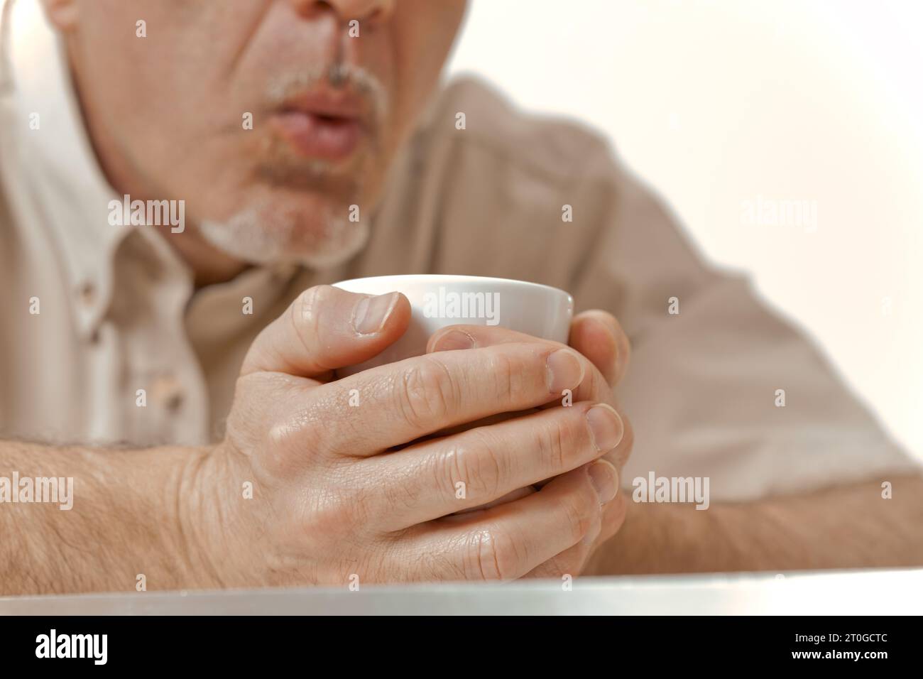 Inmitten der kalten Umarmung eines Wintermorgens bietet die Sonne wenig Entspannung. Ein alter Mann mit einem nicht erkennbaren Gesicht hält seinen Kaffee fest und bläst aus Stockfoto