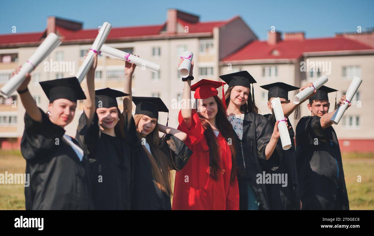 Junge Absolventen posieren und winken Diplome in den Händen auf der Straße. Stockfoto