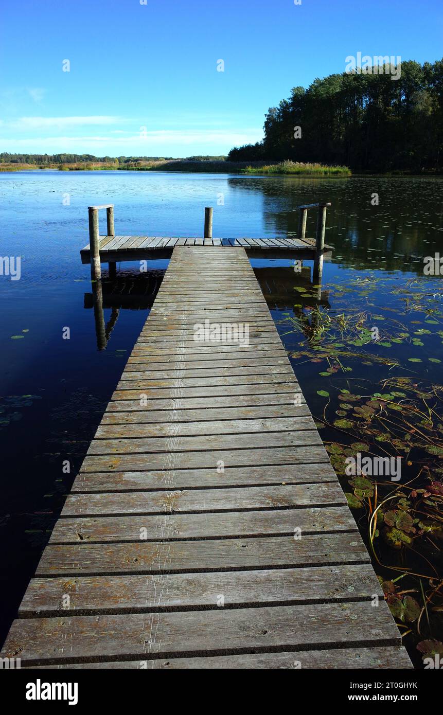 Lange Holzbrücke im See mit ruhigem Wasser und blauem Himmel in Schweden, Skandinavien, Europa. Friedliches Außenbild auf dem Malaren See in Vastmanland Stockfoto